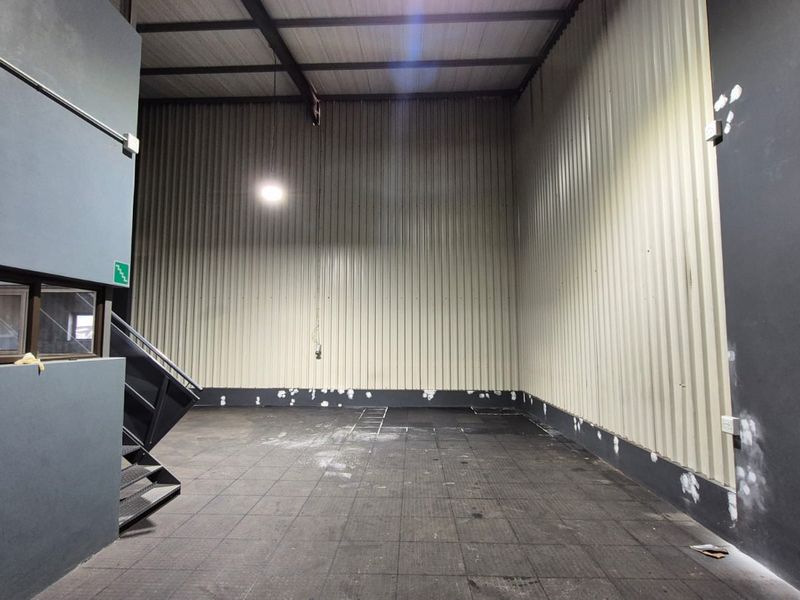 Spacious industrial utility area featuring high ceilings with exposed steel trusses, corrugated metal wall cladding, and a metal staircase.