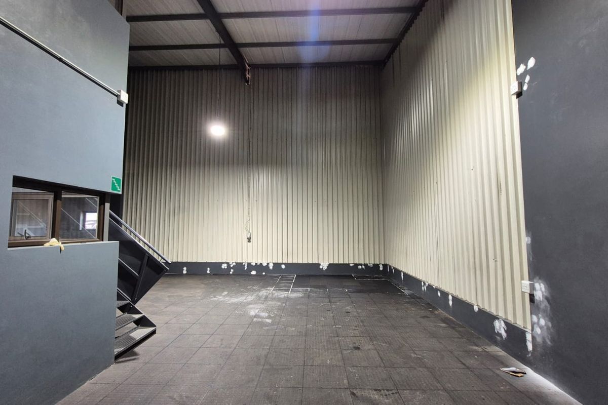 Spacious industrial utility area featuring high ceilings with exposed steel trusses, corrugated metal wall cladding, and a metal staircase.