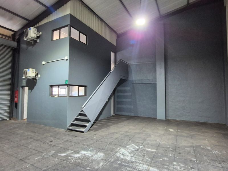Spacious industrial warehouse unit featuring a roller shutter door, high ceilings, and a built-in mezzanine office structure with staircase access.