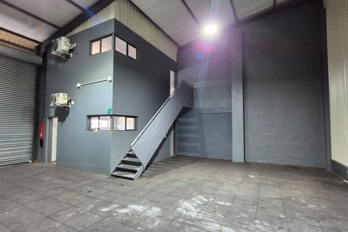 Spacious industrial warehouse unit featuring a roller shutter door, high ceilings, and a built-in mezzanine office structure with staircase access.