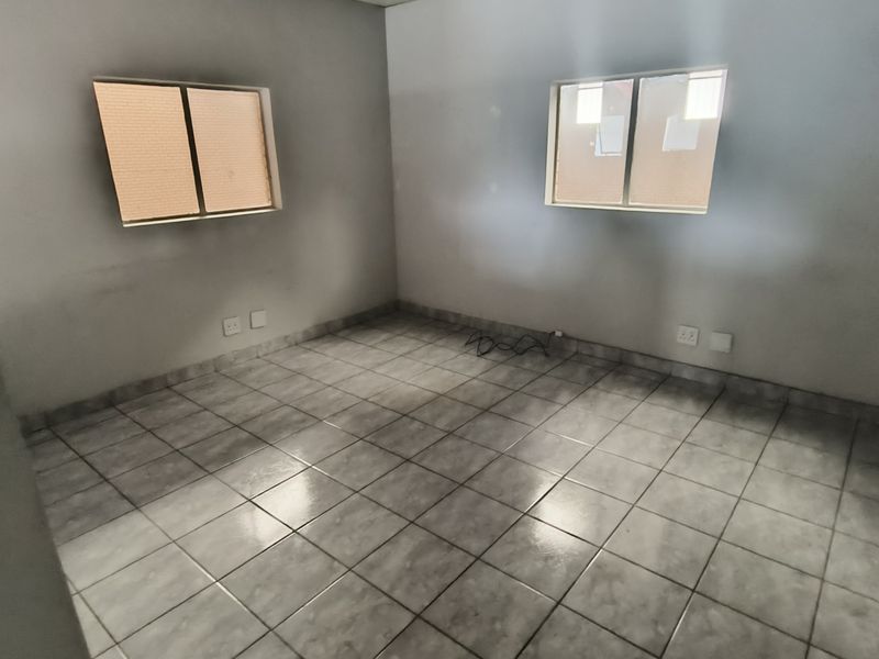 An empty bedroom featuring tiled flooring and two sliding windows, providing a blank canvas for potential industrial or office space customization.