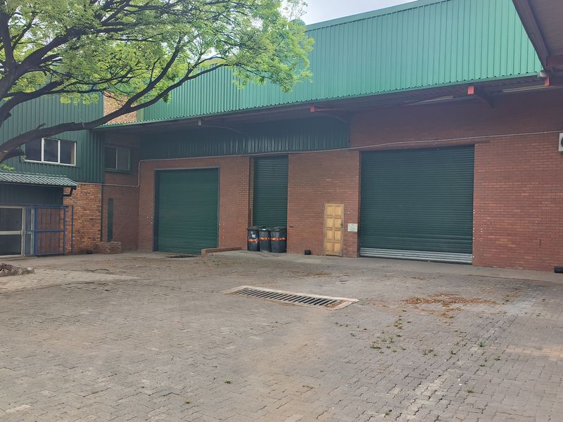 Rear industrial yard featuring brick facade, multiple roller shutter doors, metal roof cladding, and paved access area with drainage.