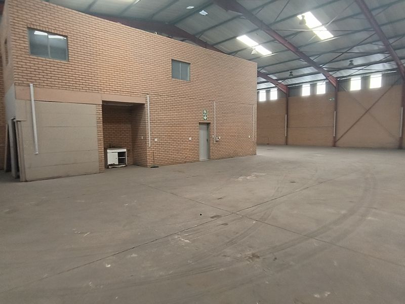 Spacious industrial warehouse featuring high ceilings with exposed steel trusses, concrete flooring, roller shutter access, and integrated brick office or utility block.