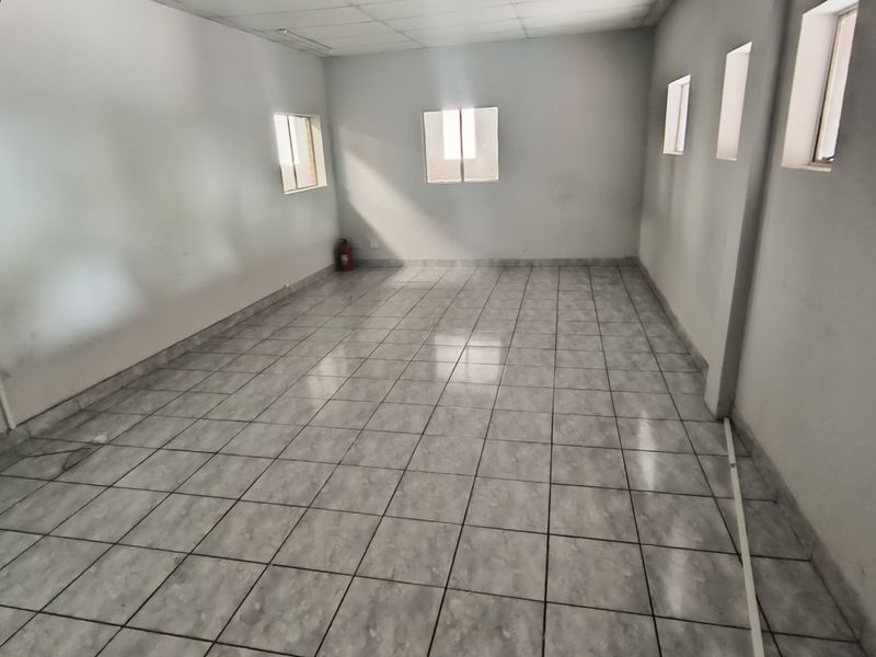 A vacant, open-plan office space featuring tiled flooring, a suspended ceiling, and multiple windows providing natural light.
