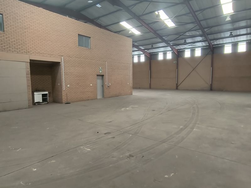 Spacious industrial warehouse unit featuring high ceilings with exposed steel trusses, skylights, durable concrete flooring, and facebrick wall construction.