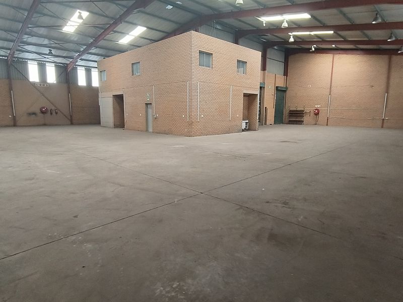 Spacious industrial warehouse featuring high ceilings with exposed steel trusses, durable concrete flooring, and a central brick office or storage structure.