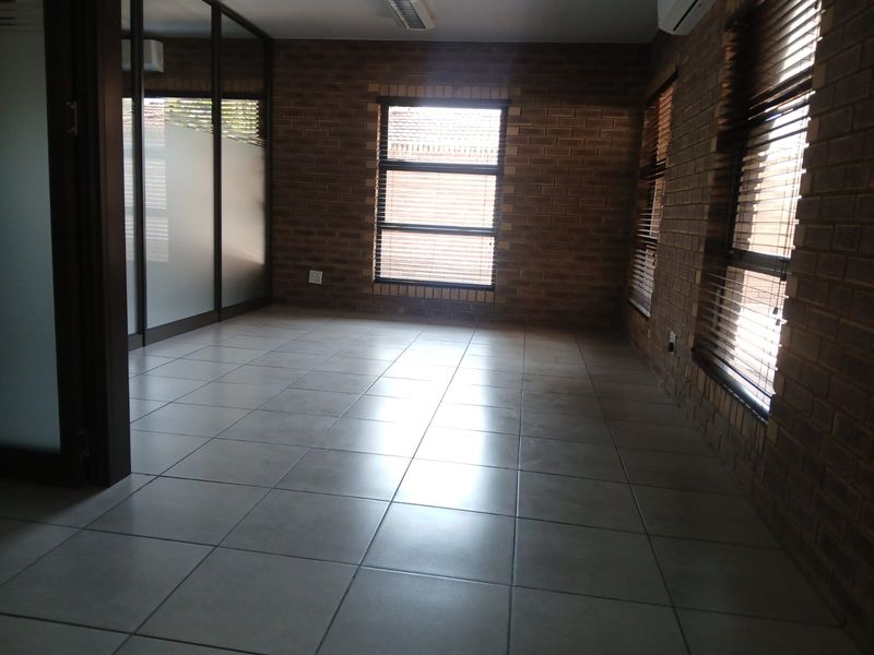 A vacant commercial office space featuring exposed brick walls, ceramic tiled flooring, and a glass partition wall with integrated air conditioning.