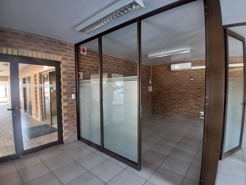 A vacant commercial office space featuring exposed brick walls, glass partitions, tiled flooring, and a wall-mounted air conditioning unit.