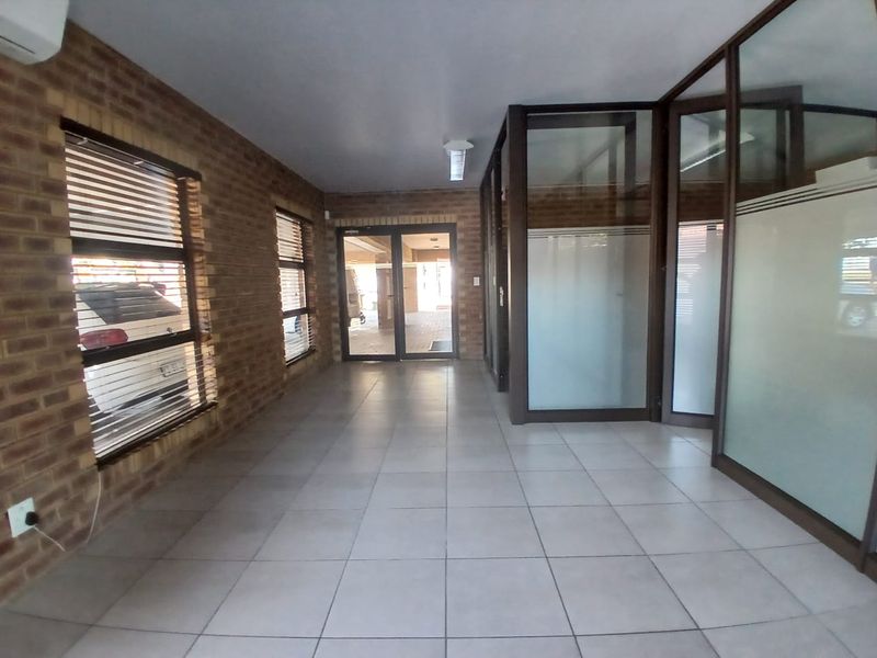 A spacious commercial hallway featuring exposed brick walls, tiled flooring, and modern glass partitions, providing a professional and well-lit entrance area.