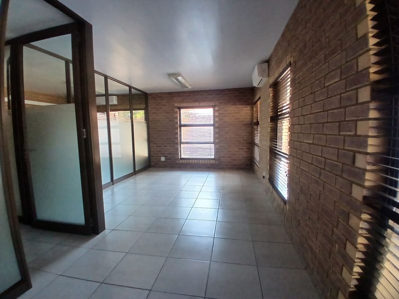 A vacant commercial office space featuring exposed brick walls, tiled flooring, and glass partitions, providing a professional and well-lit work environment.