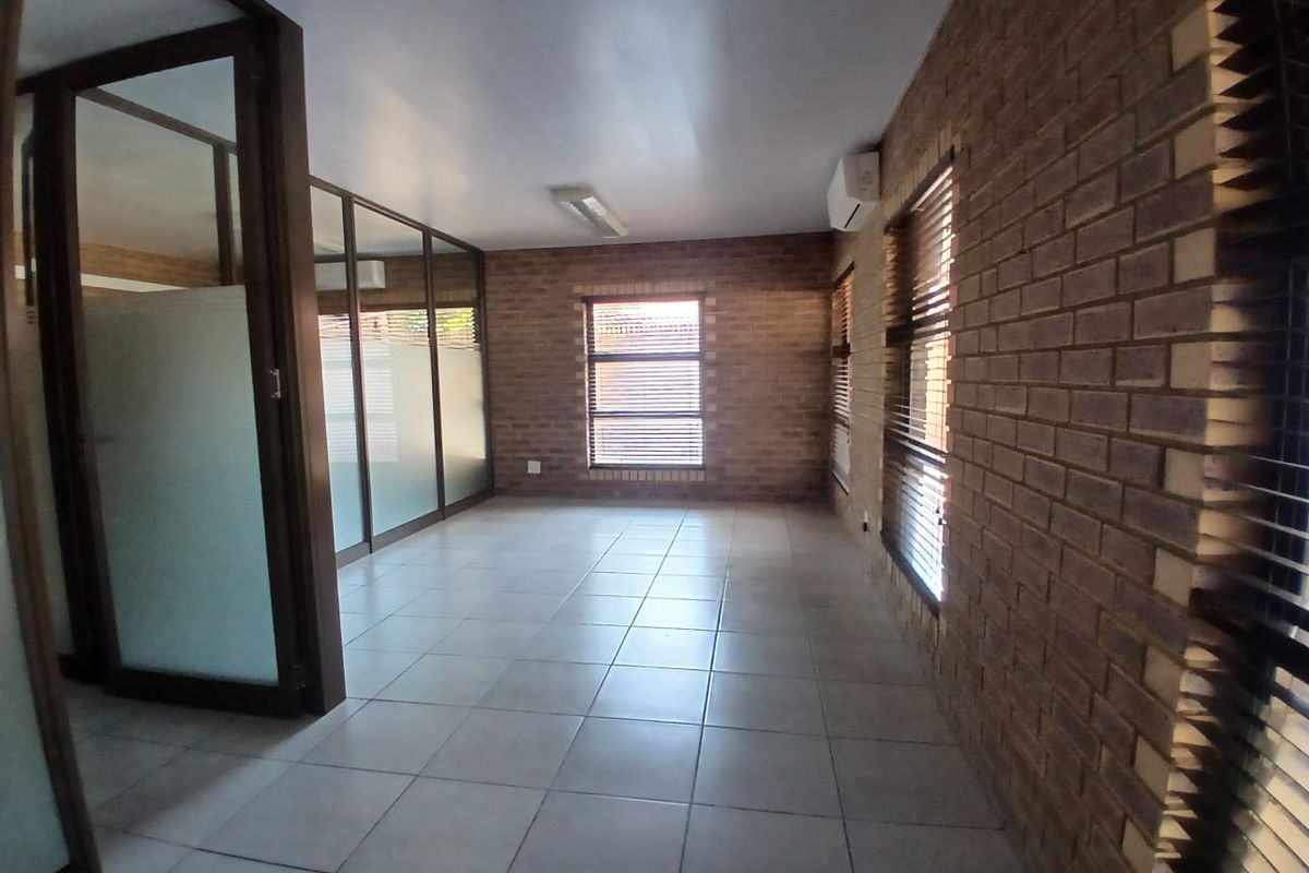 A vacant commercial office space featuring exposed brick walls, tiled flooring, and glass partitions, providing a professional and well-lit work environment.