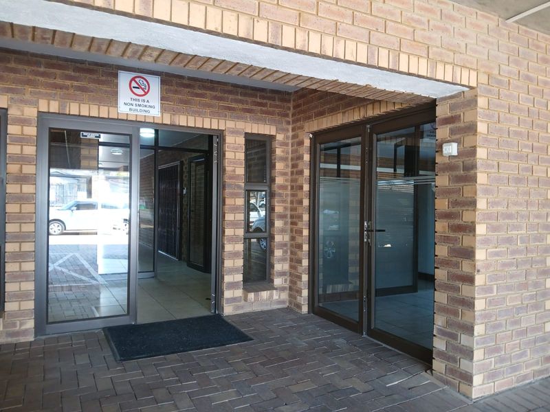 Commercial building entrance featuring face brick exterior, paved walkway, and modern aluminium-framed glass doors.