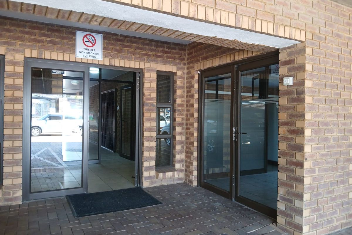 Commercial building entrance featuring face brick exterior, paved walkway, and modern aluminium-framed glass doors.