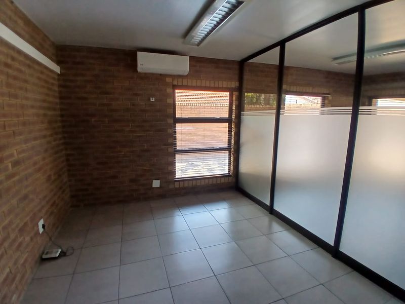 A clean, empty office space featuring exposed brick walls, tiled flooring, and a modern glass partition wall with privacy frosting.
