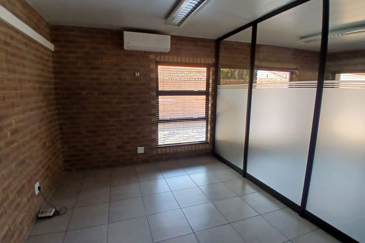 A clean, empty office space featuring exposed brick walls, tiled flooring, and a modern glass partition wall with privacy frosting.