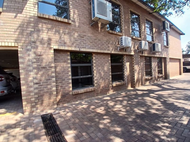 A commercial building exterior featuring a face brick facade, paved driveway, and multiple external air conditioning units mounted on the wall.