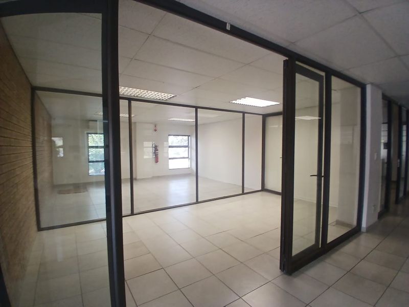 A vacant office space featuring glass partitioning, tiled flooring, and a suspended ceiling with recessed lighting, offering a clean and professional work environment.