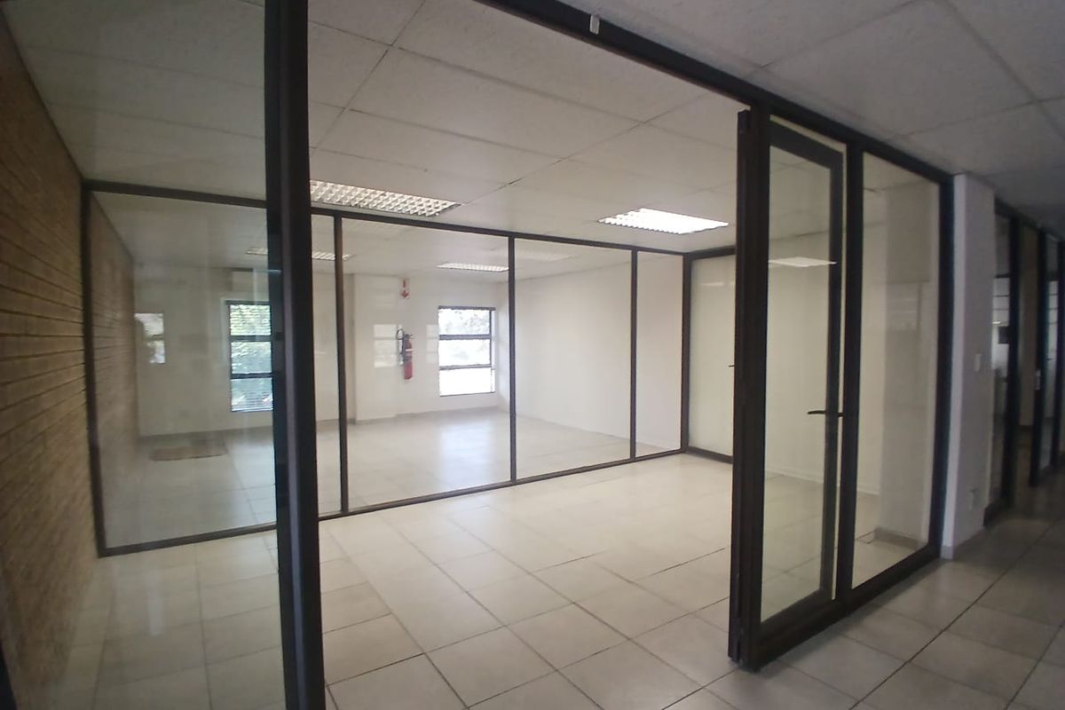 A vacant office space featuring glass partitioning, tiled flooring, and a suspended ceiling with recessed lighting, offering a clean and professional work environment.