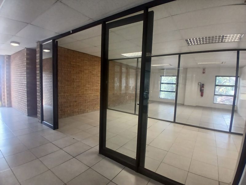 Empty office space featuring glass partitioning, exposed brick accents, ceramic tiled flooring, and suspended ceilings with recessed lighting.