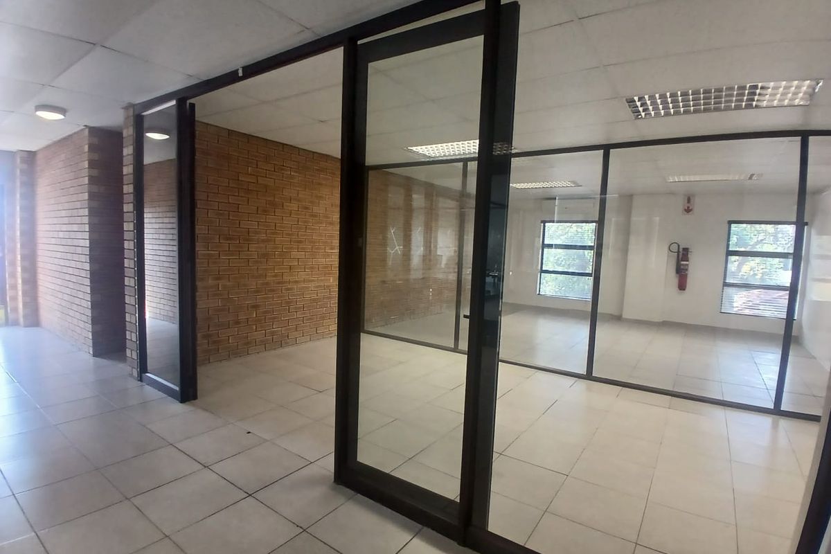 Empty office space featuring glass partitioning, exposed brick accents, ceramic tiled flooring, and suspended ceilings with recessed lighting.