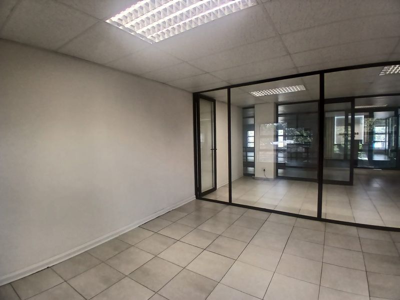 A vacant office space featuring ceramic floor tiles, a suspended ceiling with recessed lighting, and a modern glass partition wall.
