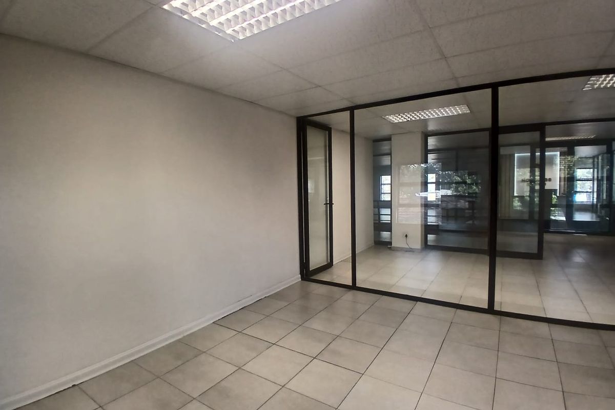 A vacant office space featuring ceramic floor tiles, a suspended ceiling with recessed lighting, and a modern glass partition wall.