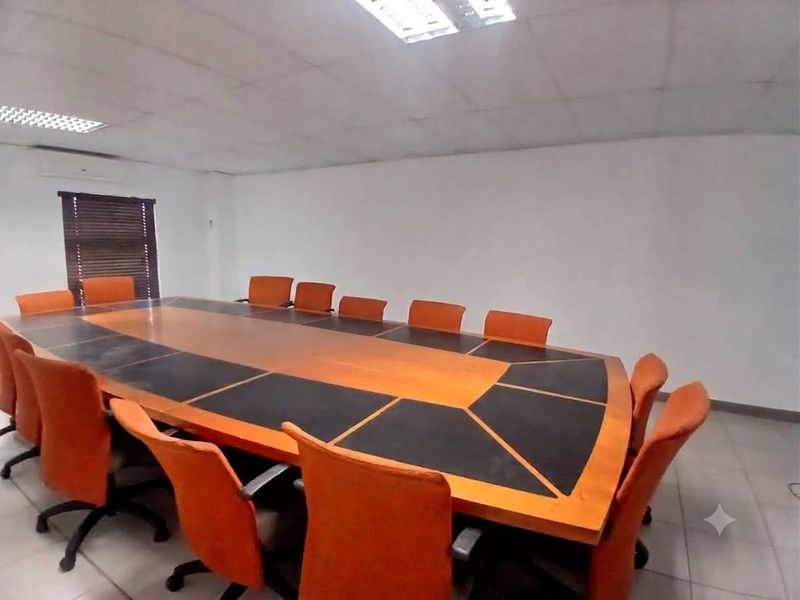 A functional office meeting room featuring a large conference table, suspended ceiling with recessed lighting, and wall-mounted air conditioning.