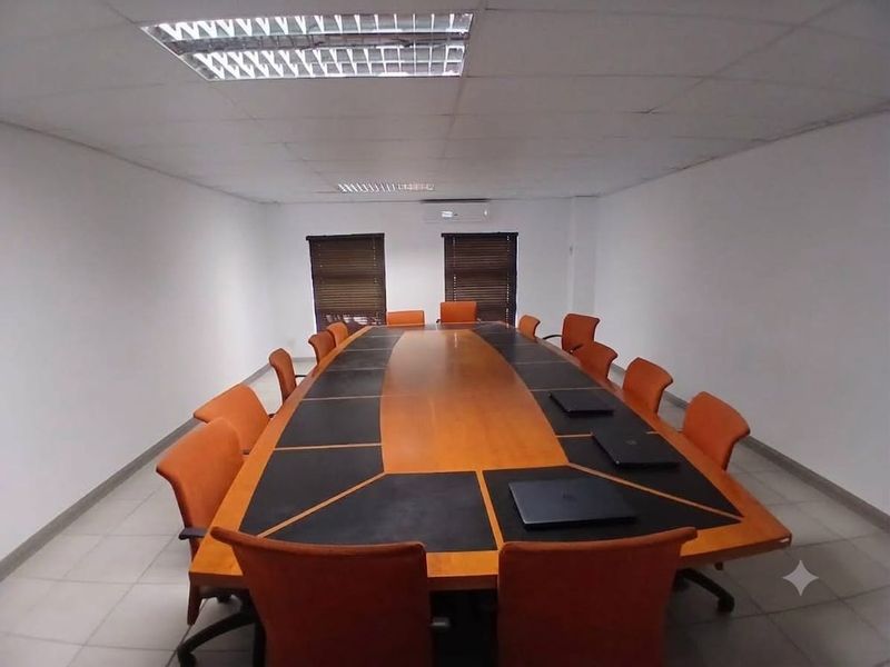 A functional office boardroom featuring a large central conference table, suspended ceiling with recessed lighting, and split-system air conditioning.