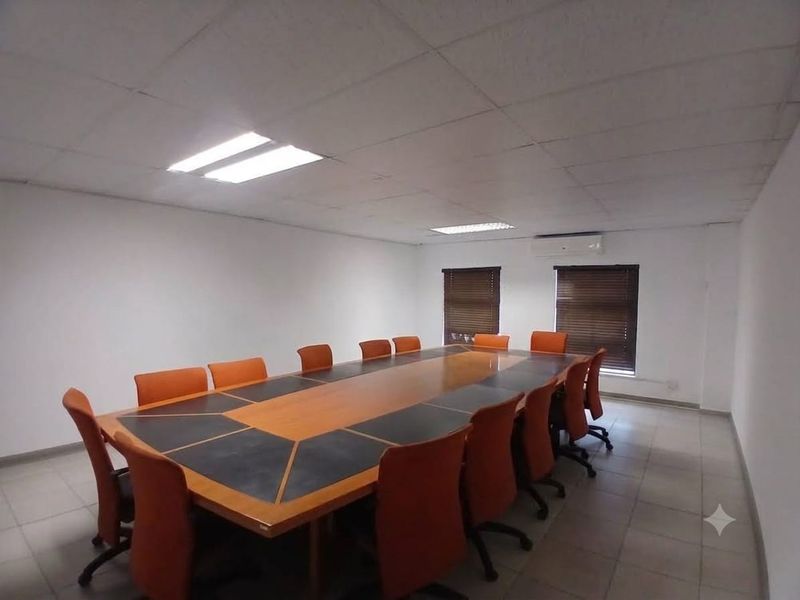 A functional office boardroom featuring a large conference table, suspended ceiling with recessed lighting, tiled floors, and wall-mounted air conditioning.