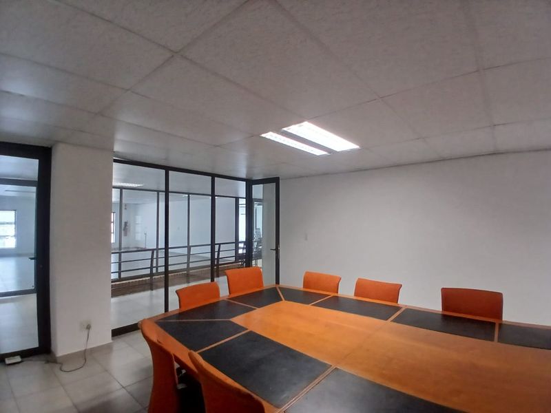 A functional office meeting room featuring a large conference table, suspended ceiling with recessed lighting, and a glass partition wall overlooking an adjacent space.