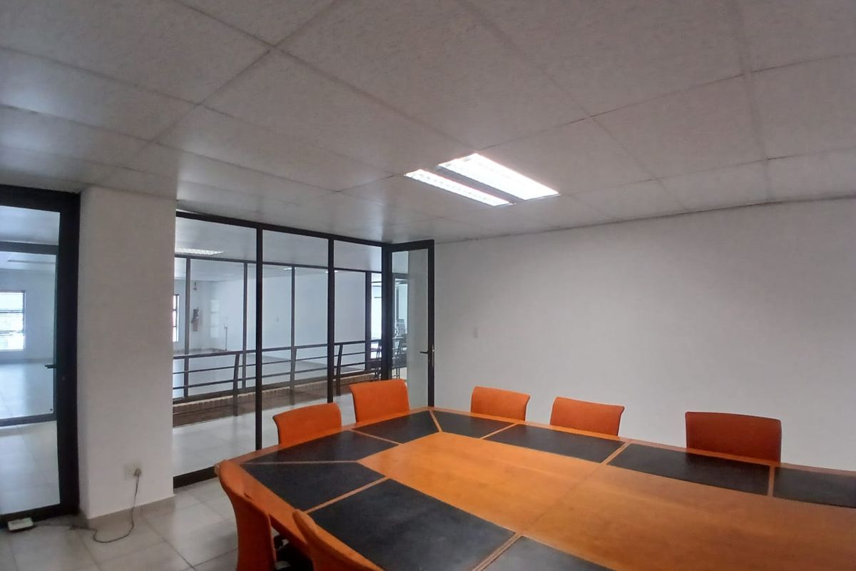 A functional office meeting room featuring a large conference table, suspended ceiling with recessed lighting, and a glass partition wall overlooking an adjacent space.