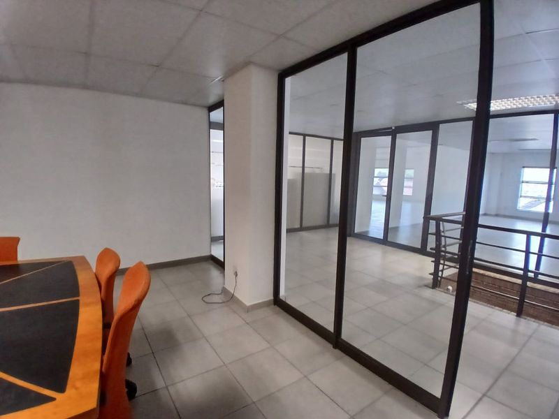 An office space featuring glass partition walls, tiled flooring, and a suspended ceiling, providing a professional and open work environment.