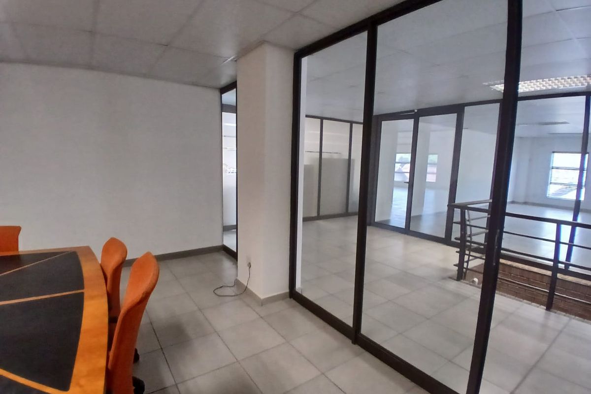 An office space featuring glass partition walls, tiled flooring, and a suspended ceiling, providing a professional and open work environment.