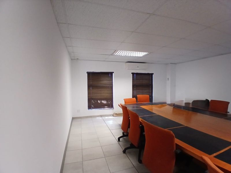 A functional office meeting room featuring tiled flooring, a suspended ceiling with recessed lighting, and a wall-mounted air conditioning unit.