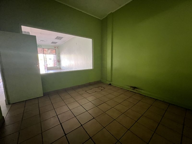 An empty office space featuring tiled flooring and an internal service window, requiring cosmetic updates to the walls and flooring.