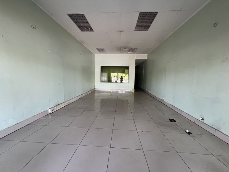 An empty commercial retail or office space featuring tiled flooring, recessed ceiling lights, and a service window, requiring cosmetic updates.