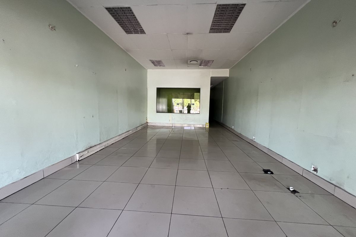 An empty commercial retail or office space featuring tiled flooring, recessed ceiling lights, and a service window, requiring cosmetic updates.