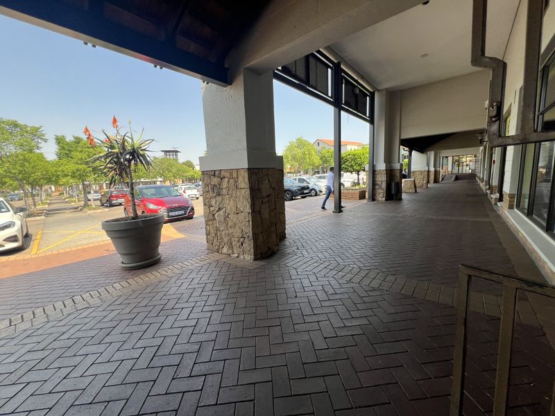 A covered outdoor walkway featuring stone-clad pillars and brick paving, providing pedestrian access along the front of the commercial property.