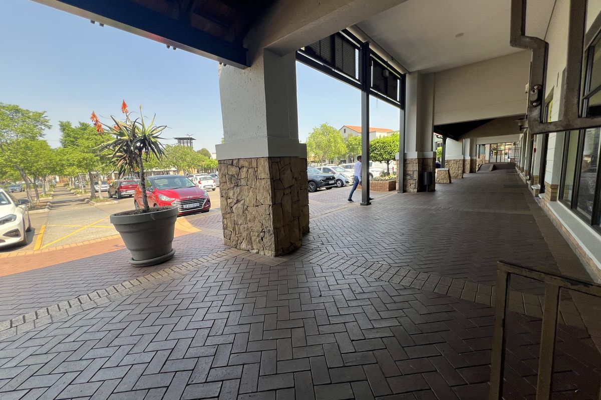 A covered outdoor walkway featuring stone-clad pillars and brick paving, providing pedestrian access along the front of the commercial property.