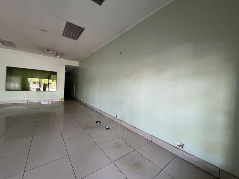 An empty commercial office space featuring tiled flooring, a suspended ceiling with recessed lighting, and a large glass window.