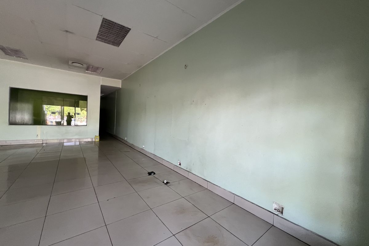 An empty commercial office space featuring tiled flooring, a suspended ceiling with recessed lighting, and a large glass window.
