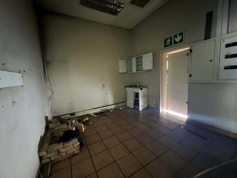 A vacant utility or kitchenette area featuring tiled flooring, built-in cabinetry, and an electrical distribution board, requiring significant refurbishment and repair.