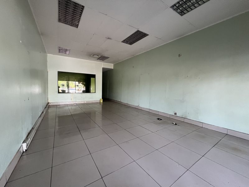 An empty commercial office space featuring tiled flooring, a suspended ceiling with recessed lighting, and an internal window.