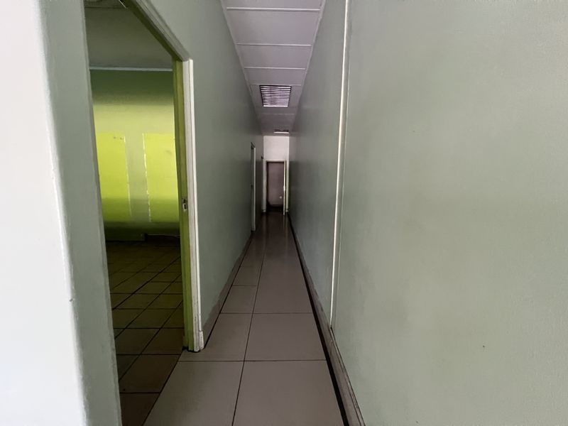 A functional commercial hallway featuring tiled flooring and a suspended ceiling, providing access to adjacent office or utility spaces.