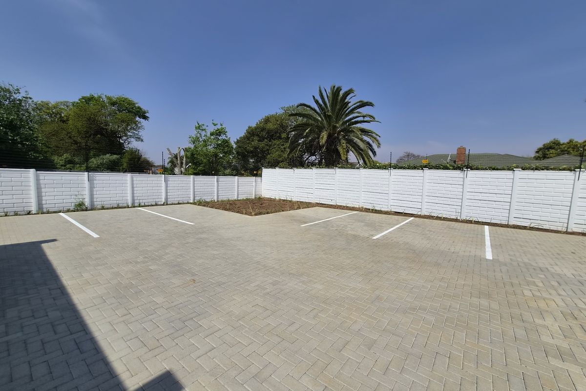 A well-maintained paved parking area featuring marked bays, enclosed by a secure precast concrete boundary wall with electric fencing.