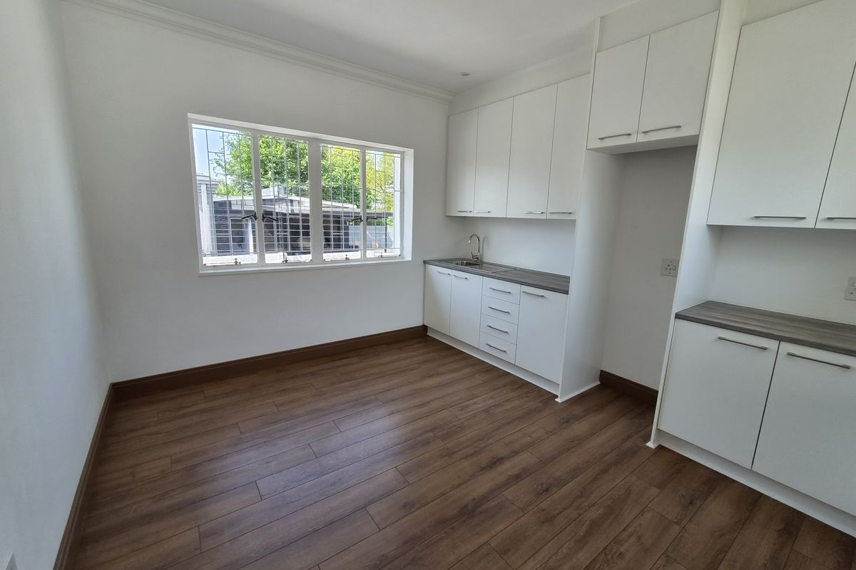 A clean, modern kitchen area featuring white built-in cabinetry, laminate countertops, a stainless steel sink, and wood-look laminate flooring.