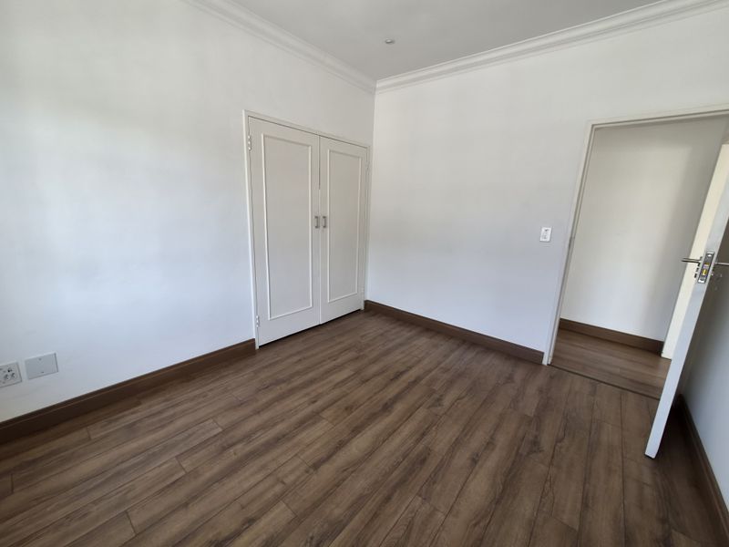 A bright, empty bedroom featuring modern laminate flooring, built-in cupboards, and clean white walls with coving detail.