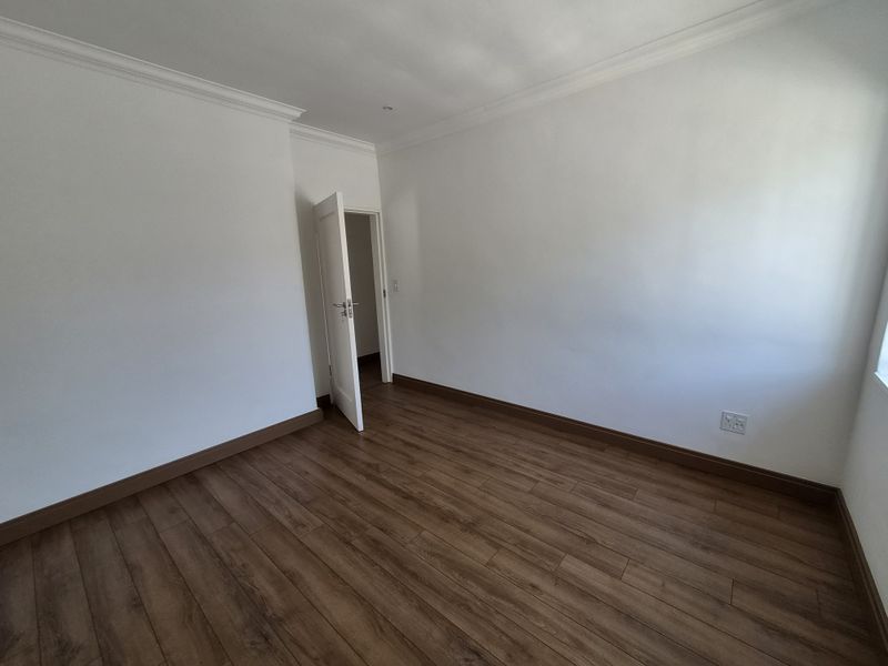 A bright, empty bedroom featuring wood-look laminate flooring, white walls, crown molding, and a single doorway leading to an adjacent space.