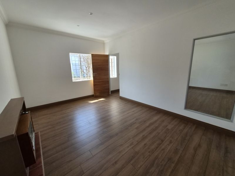 A bright, empty living room featuring modern laminate flooring, recessed lighting, and a built-in fireplace, offering a clean and versatile space.