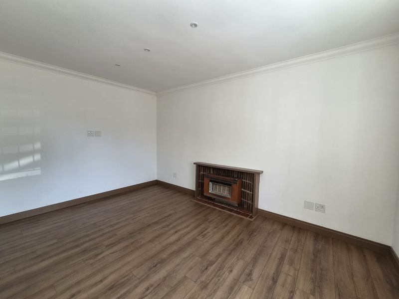 A bright, empty living room featuring laminate flooring, recessed downlights, and a built-in gas fireplace with a tiled surround.